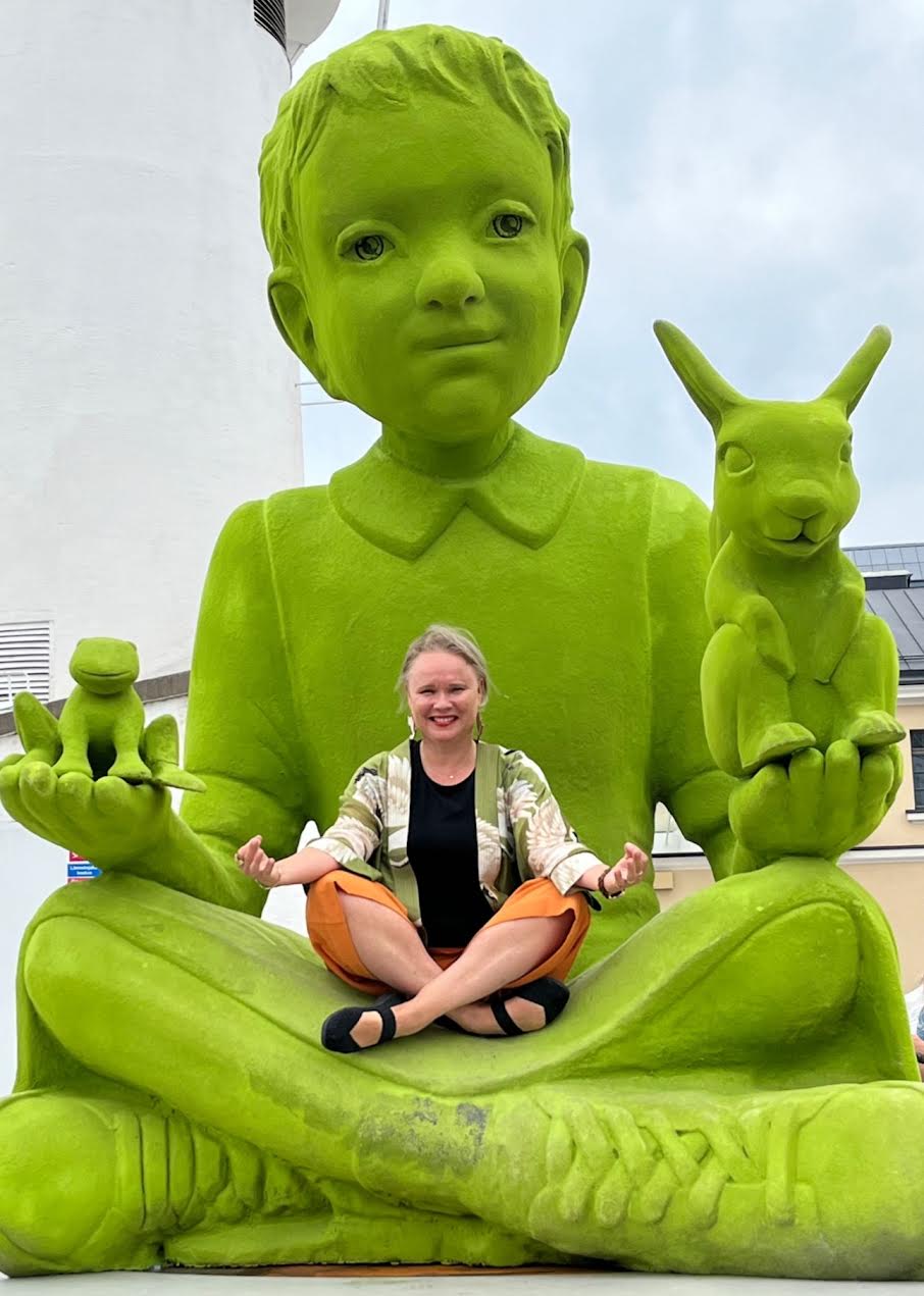 Nainen istuu risti-istunnassa suuren vihreän veistoksen sylissä.